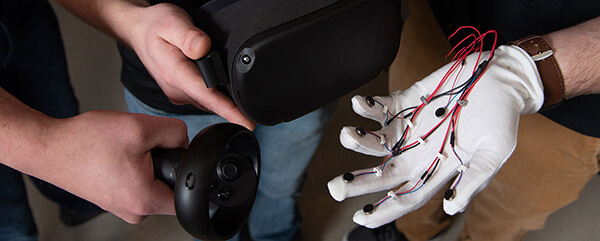 Hands interacting with a VR controller and headset, alongside a glove with wires and sensors.
